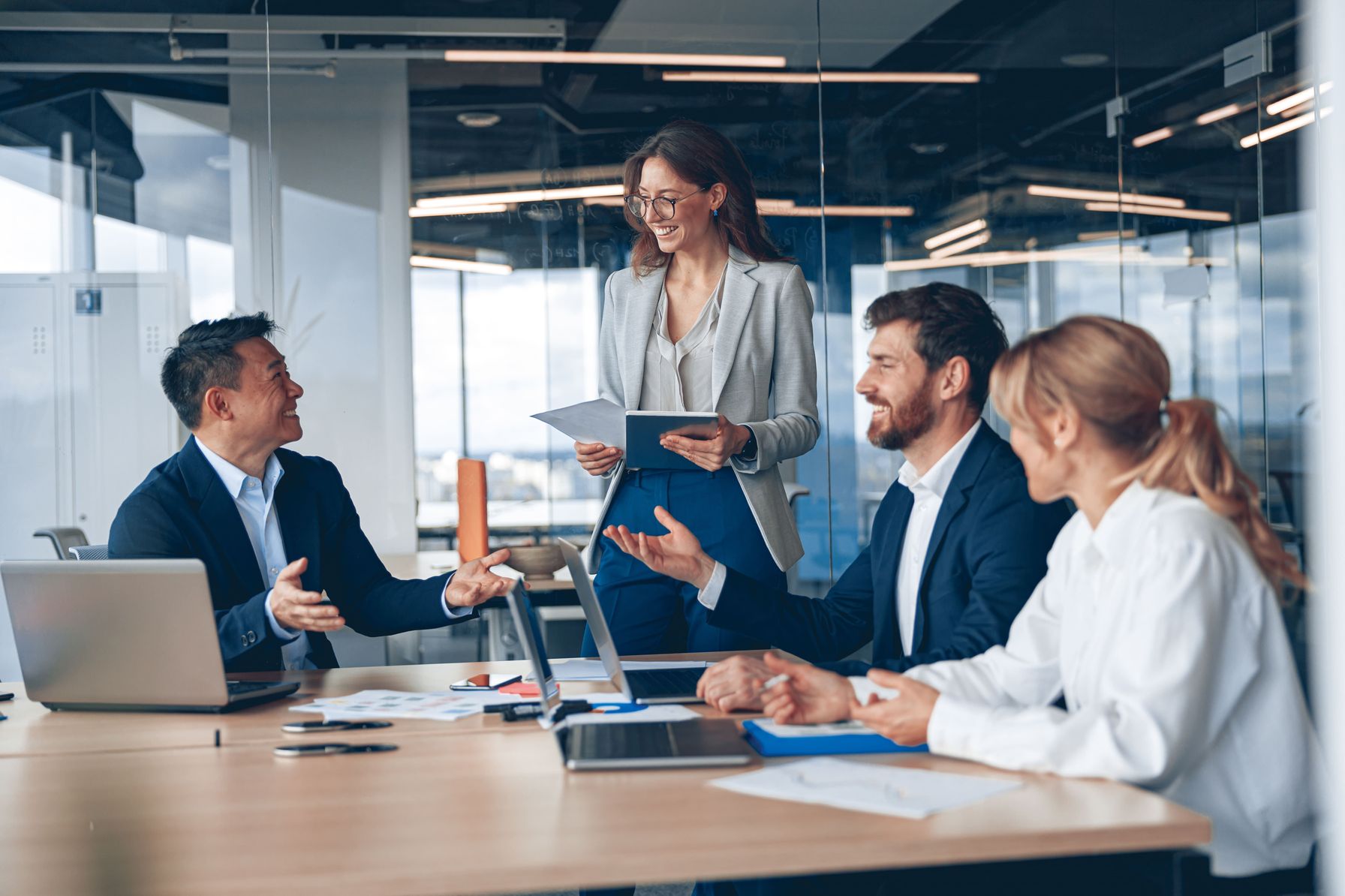 A diverse group of business professionals engaged in a discussion in a modern glass-walled office.
